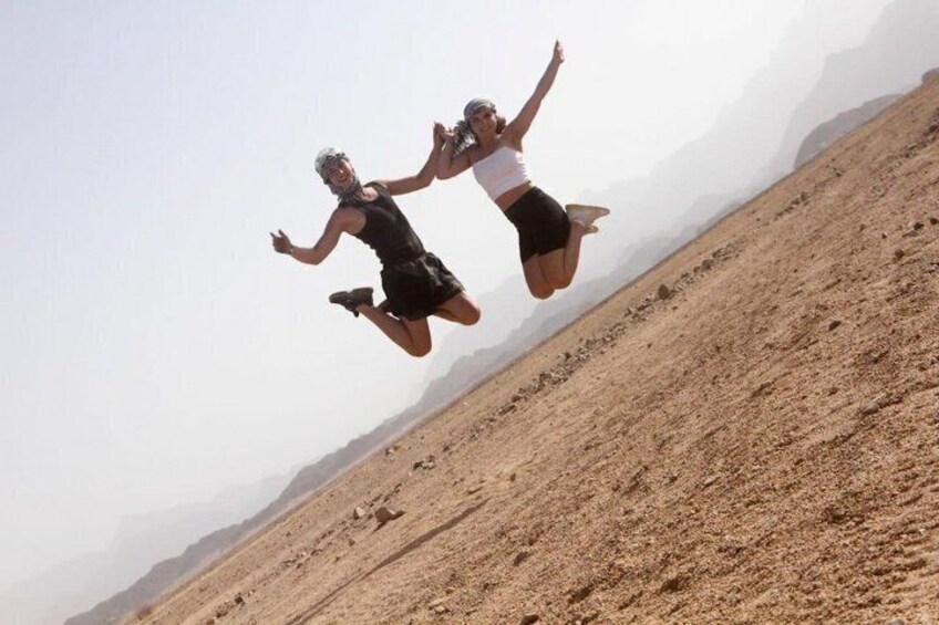 Two people jumping in mid-air on a barren, hilly landscape. 4