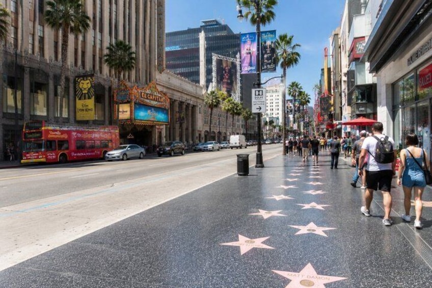 A street with palm trees, a red double-decker bus, and a sidewalk with star-shaped markings. 5