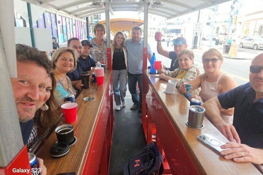 A group of people seated inside a vehicle with a wooden interior, red seats, and a metal bar. 5
