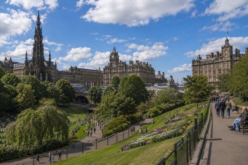 A historic building complex with a prominent tower, a well-maintained garden with a pathway, and a clear blue sky. 4
