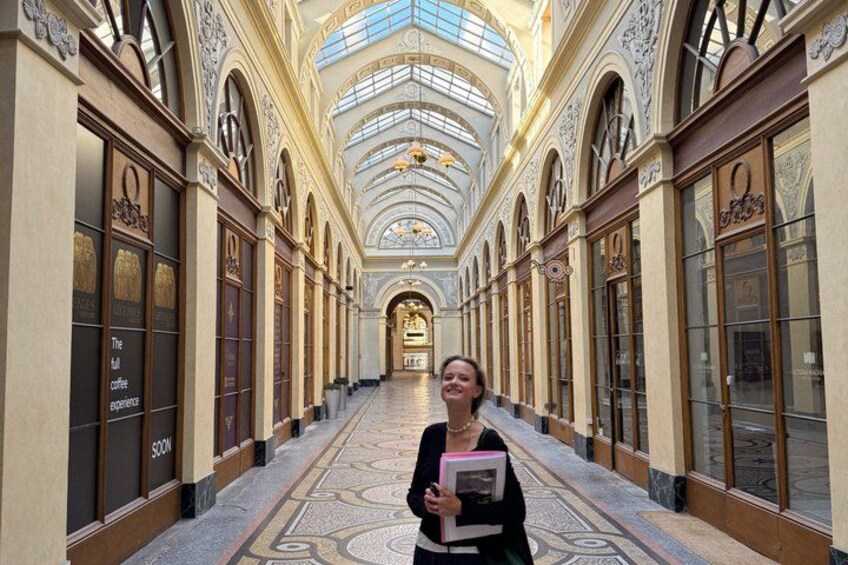 A person standing in a grand, ornately decorated hallway with arched ceilings and patterned floor tiles. 4