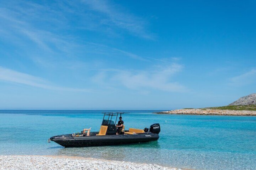 A boat on a clear turquoise sea with a rocky shoreline in the background. 1