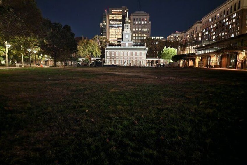 A nighttime cityscape with a large open grassy area, a historic building with a clock tower, and modern high-rise buildings. 5