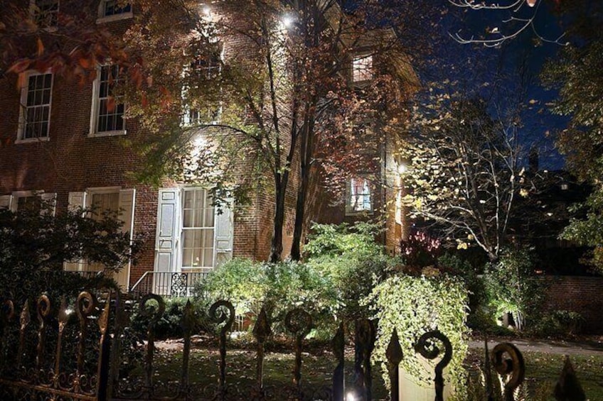 A brick building with white shutters, a metal fence, and trees with autumn leaves. 2