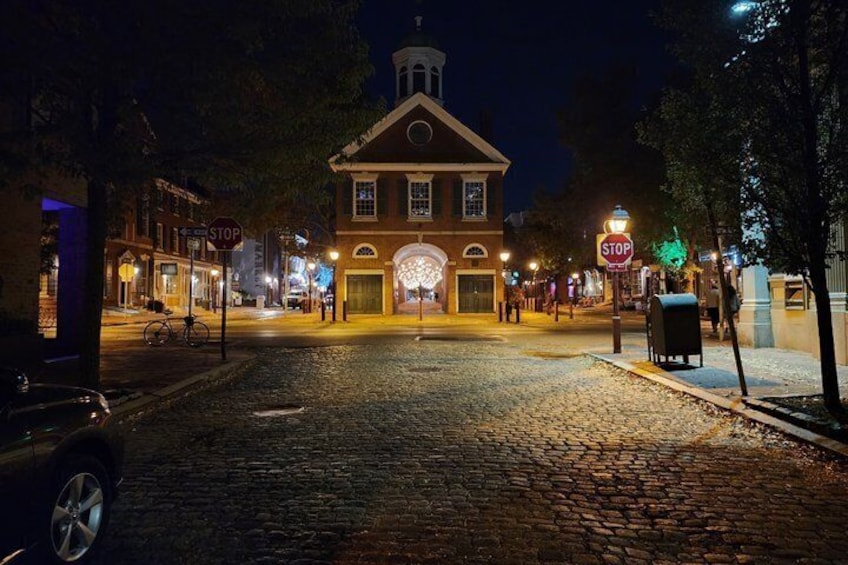 A cobblestone street at night with a historic building, illuminated stop signs, and a bicycle. 3
