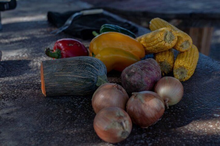 A variety of vegetables including corn, onions, and squash on a textured surface. 3
