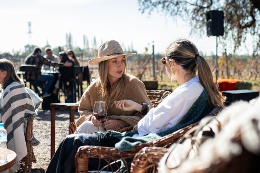 Two people sitting on wicker chairs outdoors, one holding a glass of wine. 1