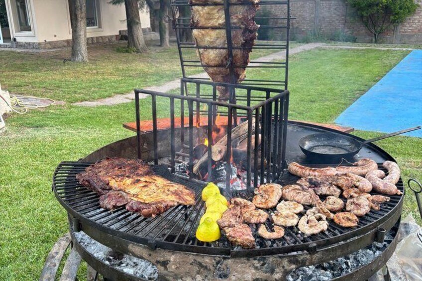 A barbecue grill with various meats cooking, a yellow bell pepper, and a hanging meat rack. 2