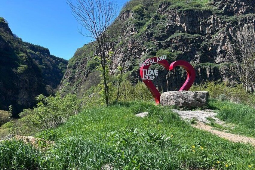 A heart-shaped sign with 'KISLAND LOVE YOU' written on it, set against a mountainous backdrop. 5