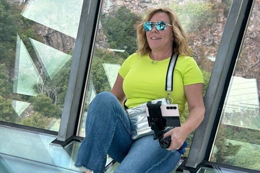 A person seated inside a transparent glass structure with a camera. 2