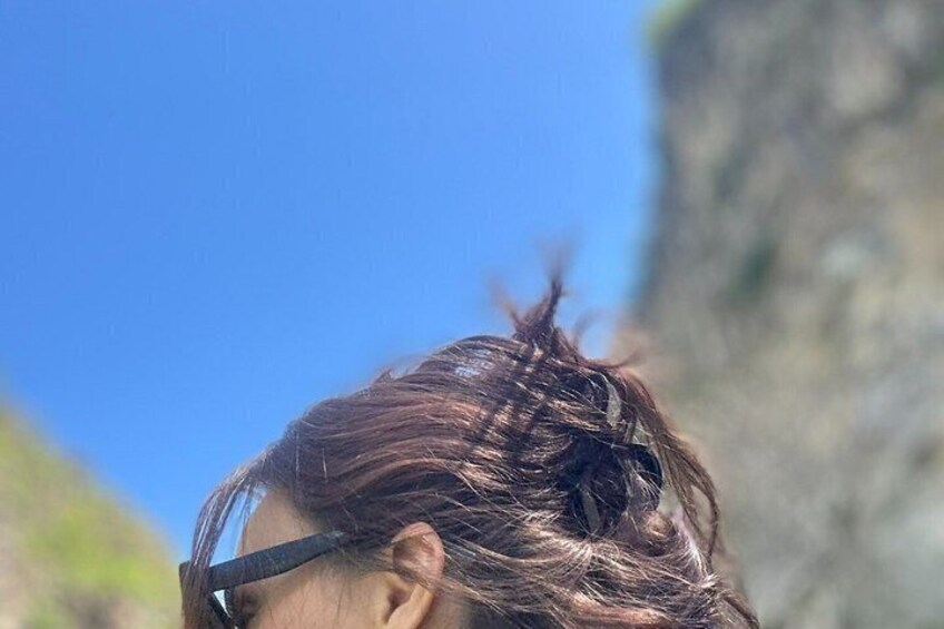 A person with dark hair against a clear blue sky and a rocky cliff. 4