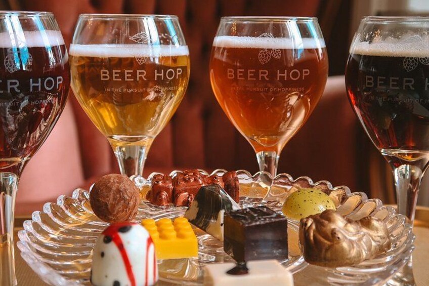 Four glasses of beer with the label 'Beer Hop' and a variety of snacks on a glass plate. 2