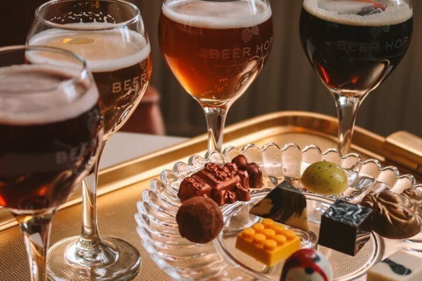 Three glasses of beer with a tray of assorted chocolates and a bottle of sauce. 1