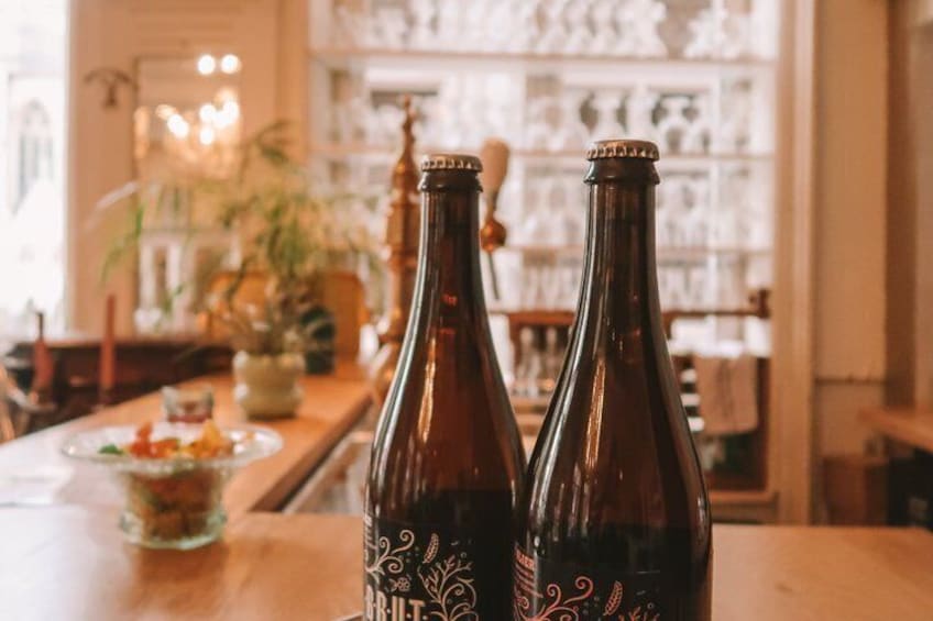 Two bottles of beer on a wooden table in a bar with shelves in the background. 3