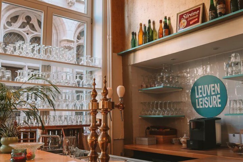 A bar with shelves of glasses and bottles, a sign reading 'Leuven Leisure,' and a decorative candle holder. 4