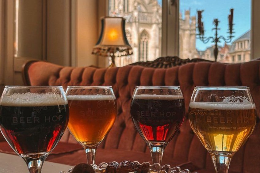 Four glasses of beer on a table with a lamp and a red sofa in the background. 2