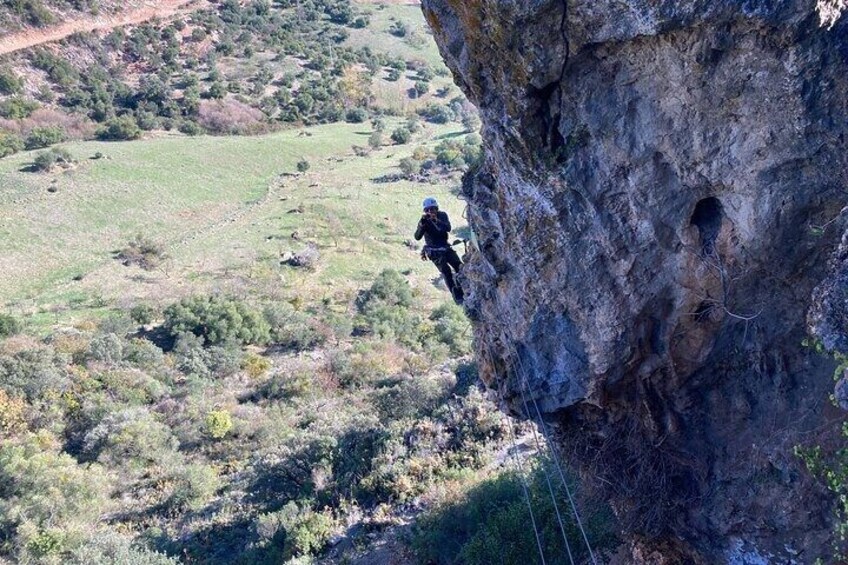A person rappelling down a rocky cliff with a rope. 5