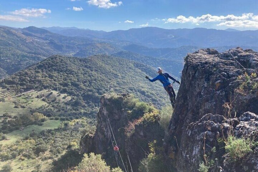 A person rappelling down a cliff with a rope, surrounded by a mountainous landscape. 4