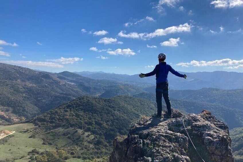 A person standing on a rocky outcrop with arms outstretched, overlooking a mountainous landscape. 1
