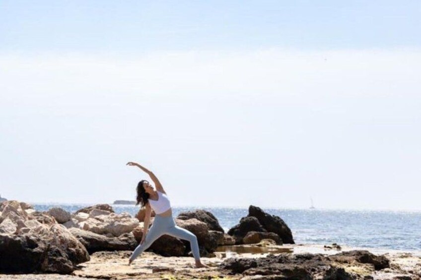 A person performing a yoga pose on a rocky beach with the ocean in the background. 3