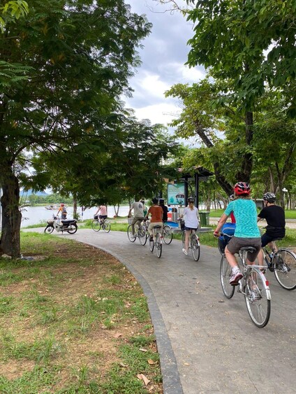 People riding bicycles on a paved path surrounded by trees and a body of water. 3