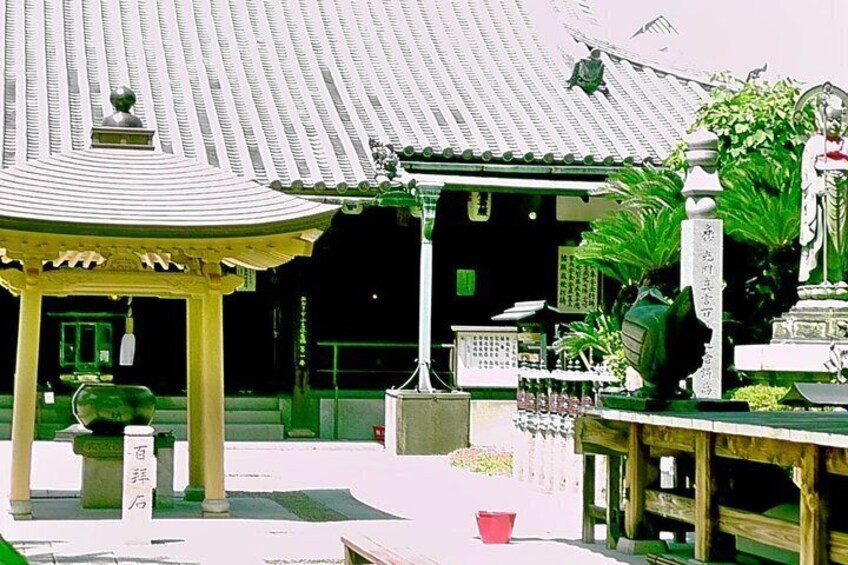 A traditional Japanese temple with a tiled roof, a stone lantern, and a statue. 3