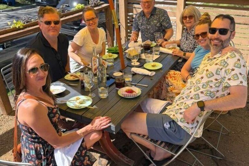 A group of people dining at an outdoor table with food and drinks. 5