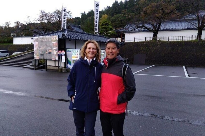 Two people standing in front of a traditional Japanese building with a tiled roof and a white wall. 3