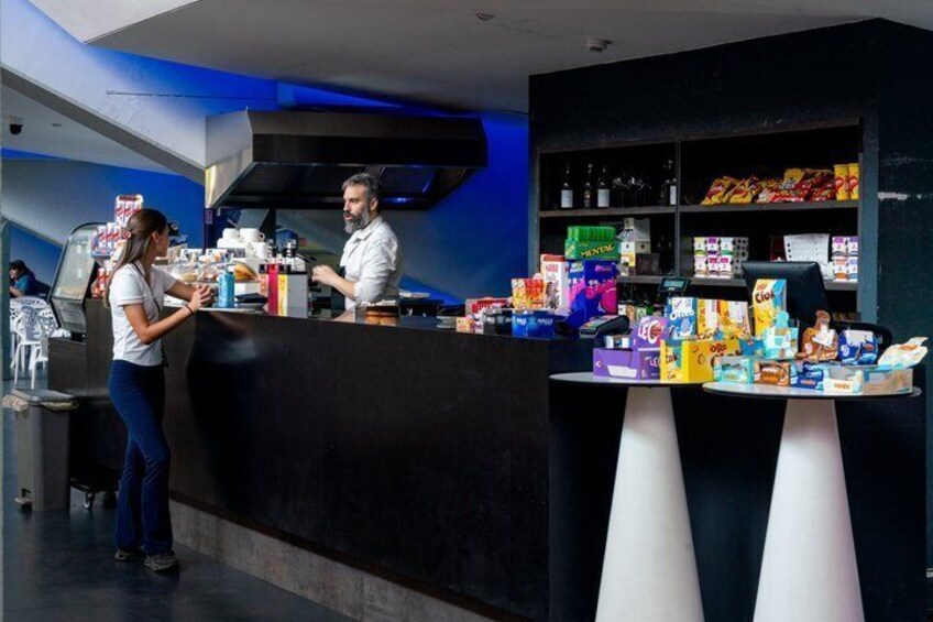 A cafe with a counter, a barista, and a customer. 2