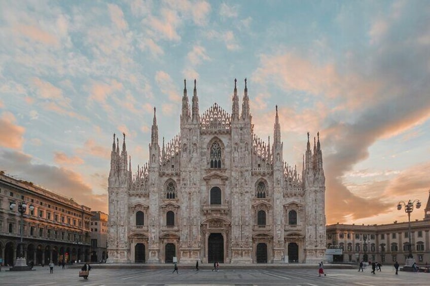 A grand cathedral with intricate Gothic architecture, a large open square in front, and a clear sky. 1