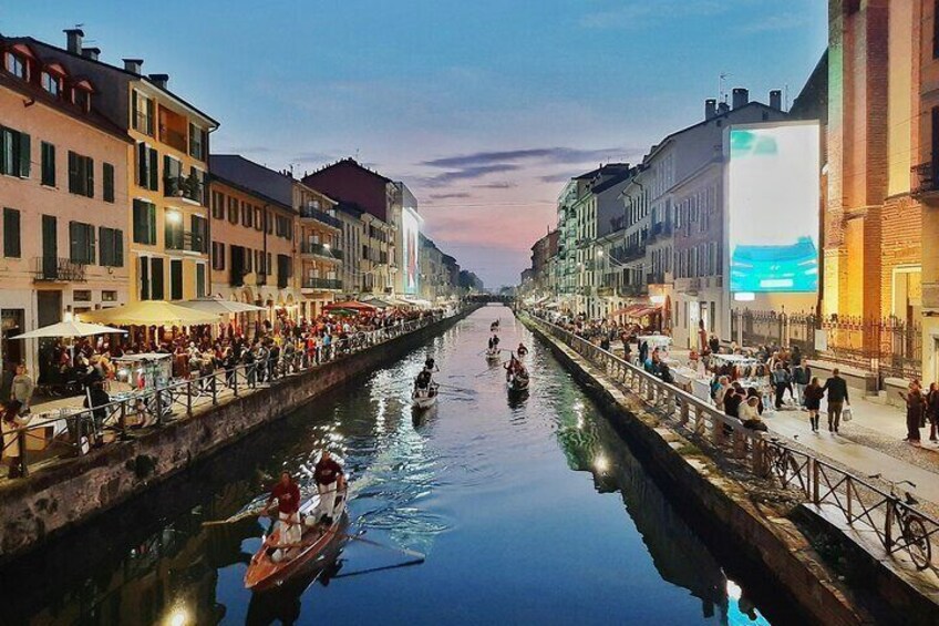 A canal with boats, people on the banks, and buildings lining the water. 2