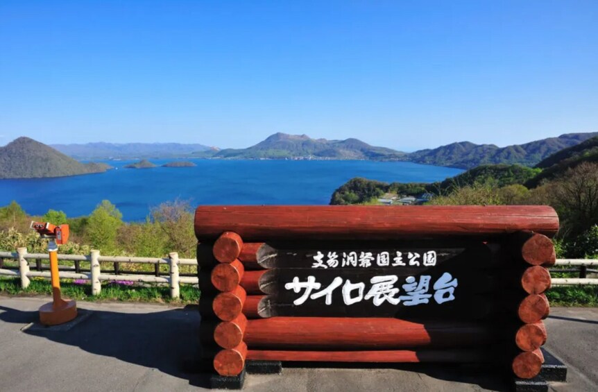 A wooden bench with Japanese text, overlooking a lake with mountains in the background. 2