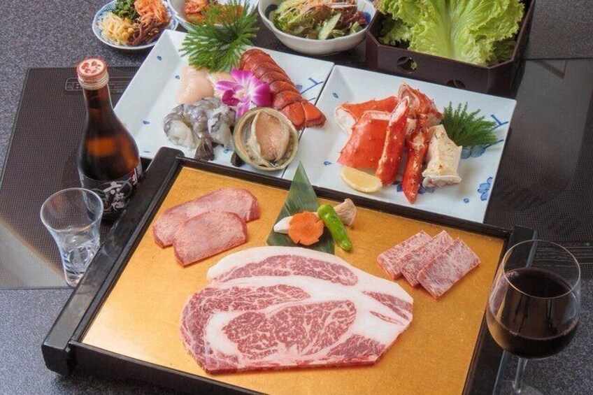 A hot plate with various meats, a bottle of sake, and a plate of seafood. 1