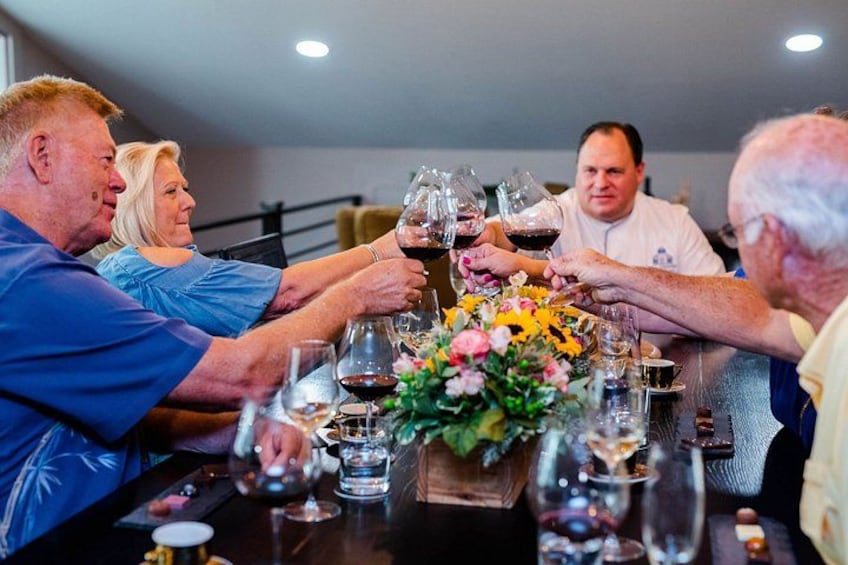 A group of people toasting with wine glasses at a dinner table with a floral centerpiece. 1