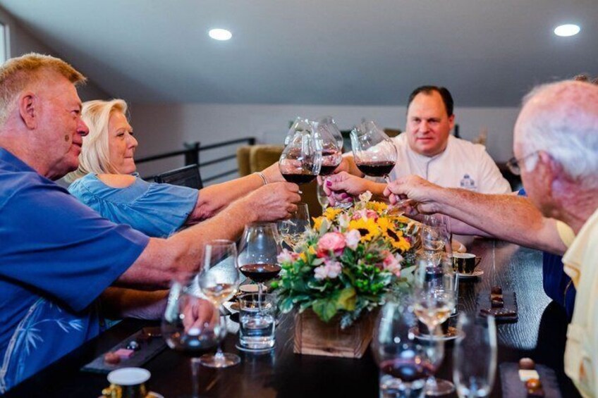 A group of people toasting with wine glasses at a dinner table with a floral centerpiece. 1