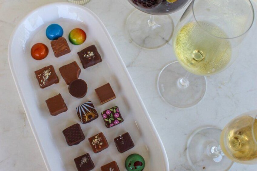 A tray of assorted chocolates and two glasses of white wine on a marble surface. 4