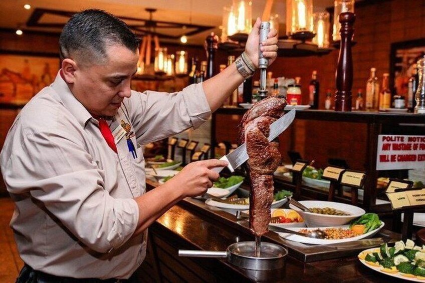 A person carving a large meat on a vertical rotisserie. 3