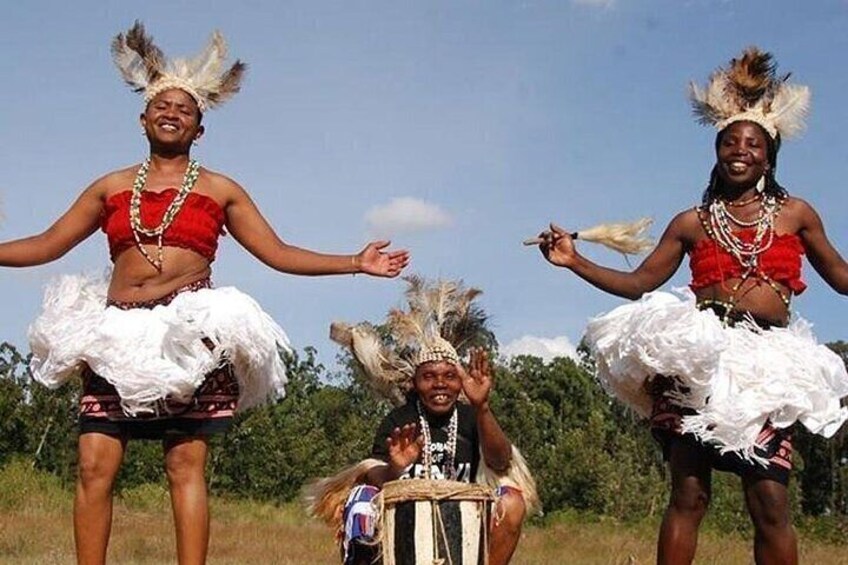 Three individuals in traditional attire with feathered headdresses, dancing in an open field. 1