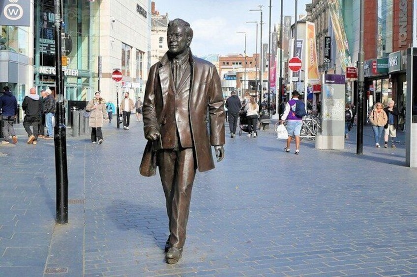 A statue of a man in a suit walking on a city street. 1