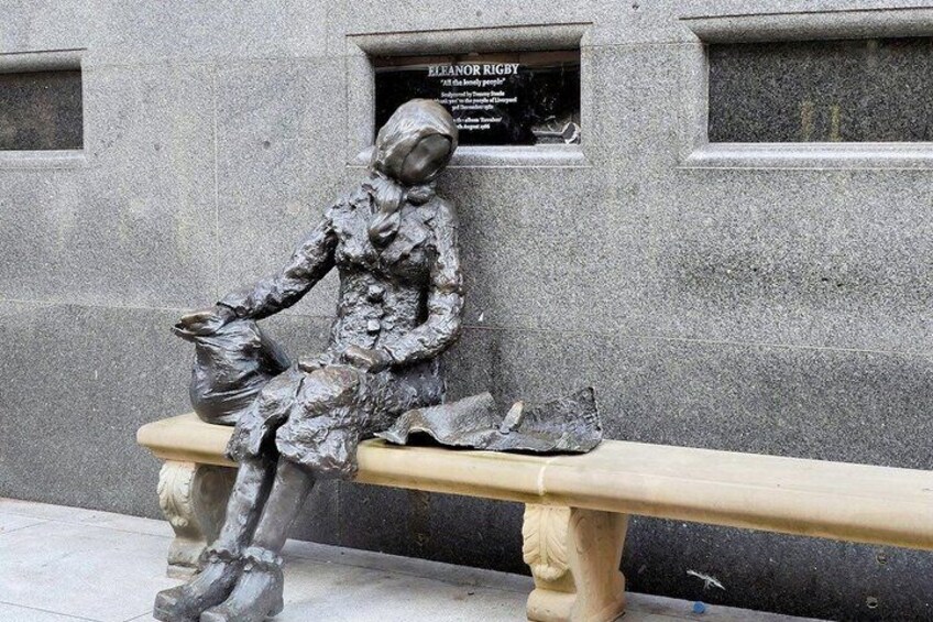 A bronze statue of a seated figure on a bench with a plaque in the background. 5