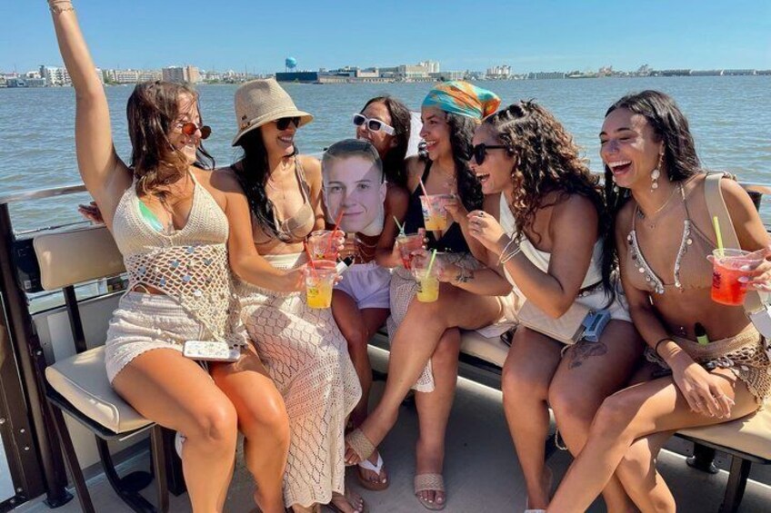 A group of people on a boat with drinks, water, and a city skyline in the background. 5