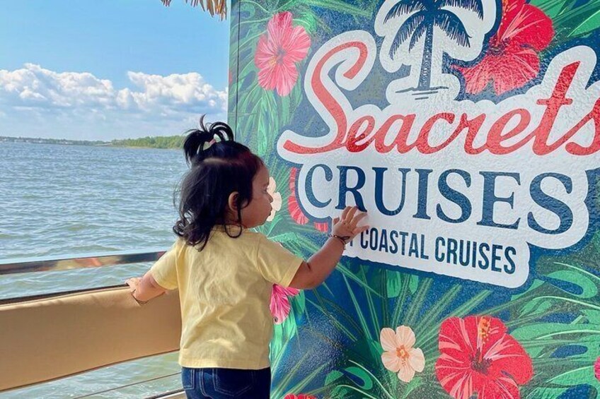 A child touching a wall with a 'Secrets Cruises' sign. 4