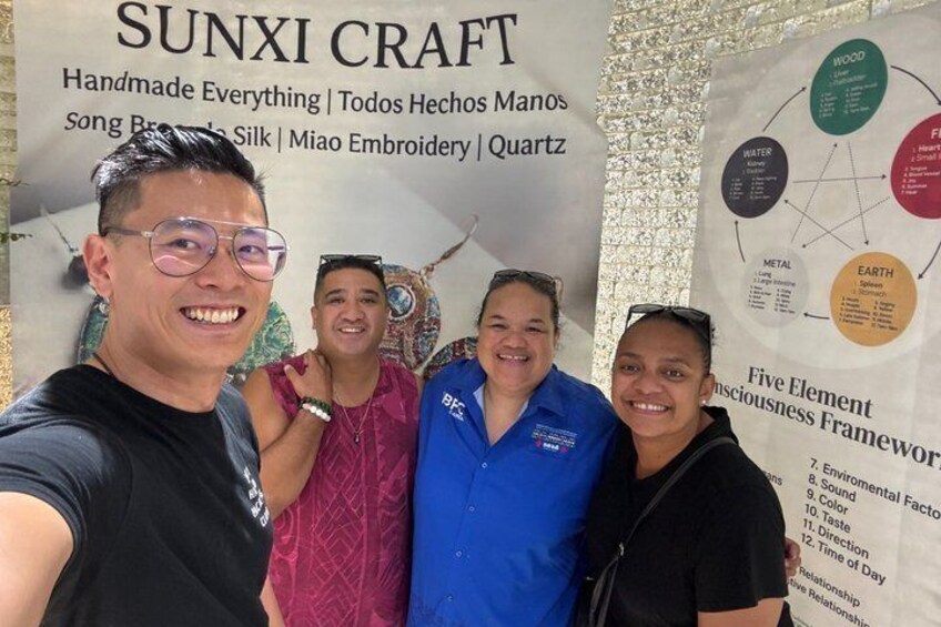 A group of people at a craft exhibition with a banner displaying 'SUNXI CRAFT' and a 'Five Element Consciousness Framework' diagram. 4