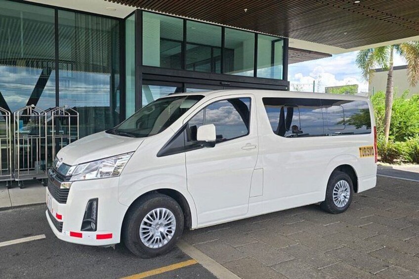 Una camioneta blanca estacionada frente a un edificio moderno con ventanas amplias y una cerca metálica. 2