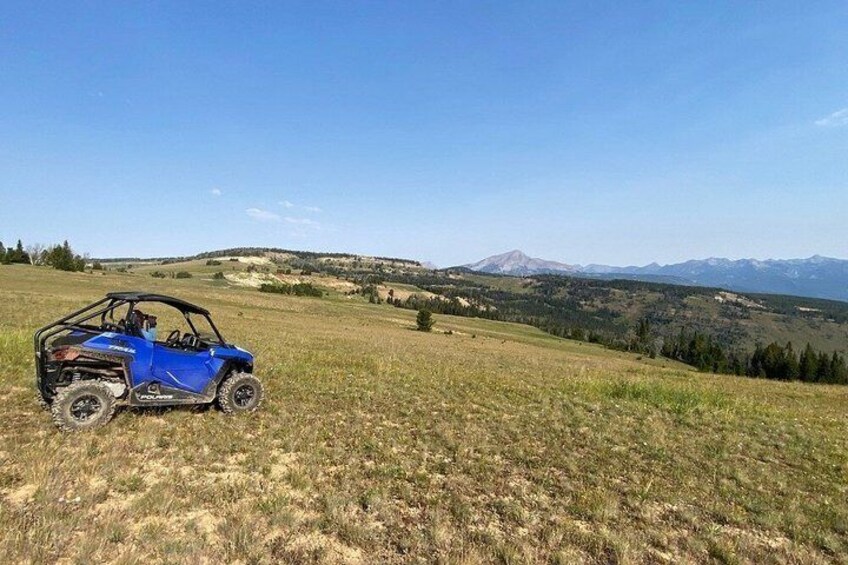A blue off-road vehicle parked on a grassy field with mountains in the background. 5