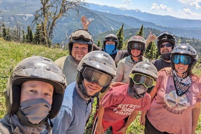 A group of people wearing helmets and protective gear, standing on a grassy hill with a mountainous landscape in the background. 4