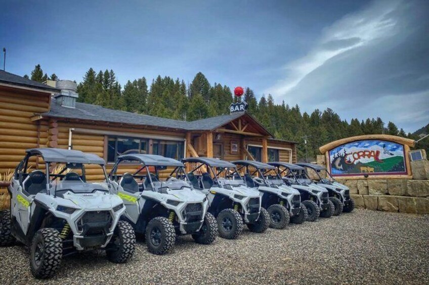A row of ATVs parked in front of a lodge with a 'BAR' sign above. 1