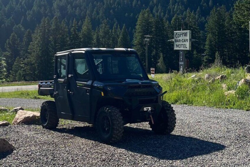 A black ATV parked on a gravel road with a sign for Corral Bar-Cafe Motel in the background. 4