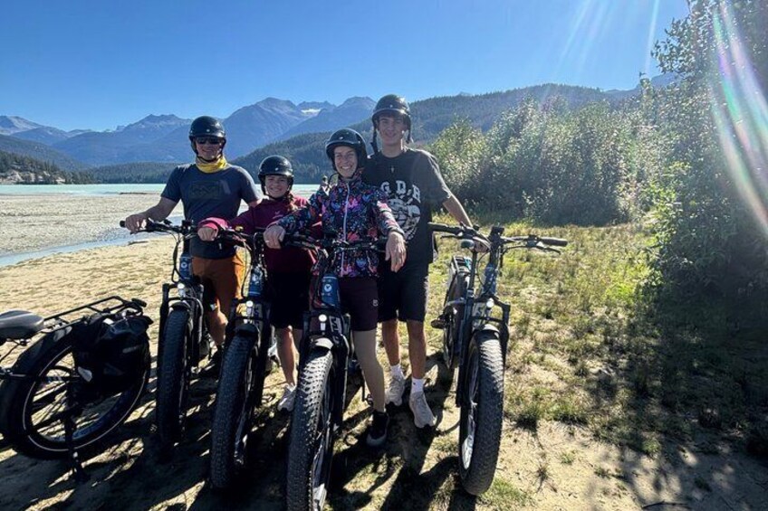 Four people on mountain bikes near a lake with mountains in the background. 2