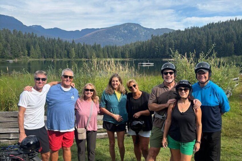 A group of people standing by a lake with mountains in the background. 4